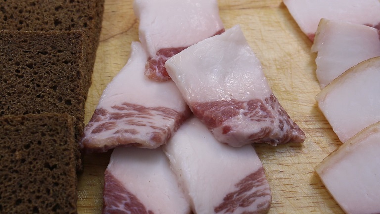 нарезанные куски соленого сала с нарезанными кусочками ржаного хлеба лежат на деревянной доске